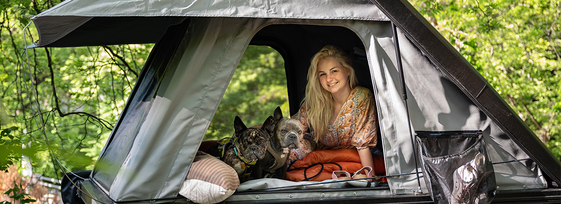 Blonde-Frau zelten mit zwei Hunden in einem Dach-Zelt auf einem Auto