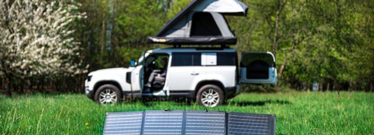 Großes weißes Auto mit Dachzelt davor Solarplatten