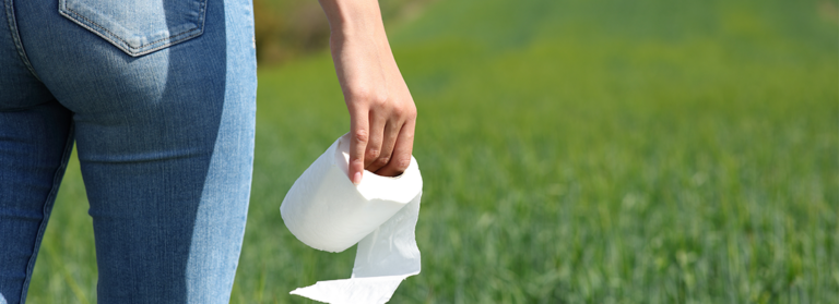 Eine Frau steht auf der Wiese und hält Klopapier in der Hand