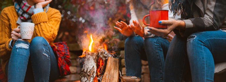 Drei weibliche Freundinnen, die um das Feuer herum sitzen, in ungezwungenen Kleidern, die sich erwärmen und kommunizieren