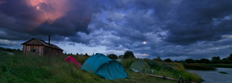 Zelten bei Gewitter. Dunkler Himmel mit Blitz und Zelte auf einer Wiese neben dem Wasser.