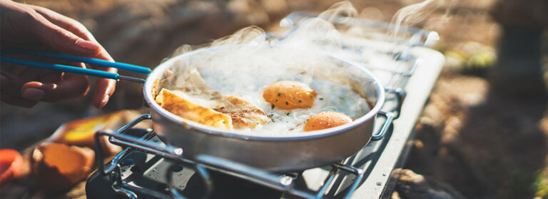 Person, die gebratene Eier im Naturcamping im Freien kocht, Herd bereiten gegrilltes Omeletfrühstück Picknick auf Metall-Herd, Tourist auf Freizeit draußen; Campingplatz-Lifestyle